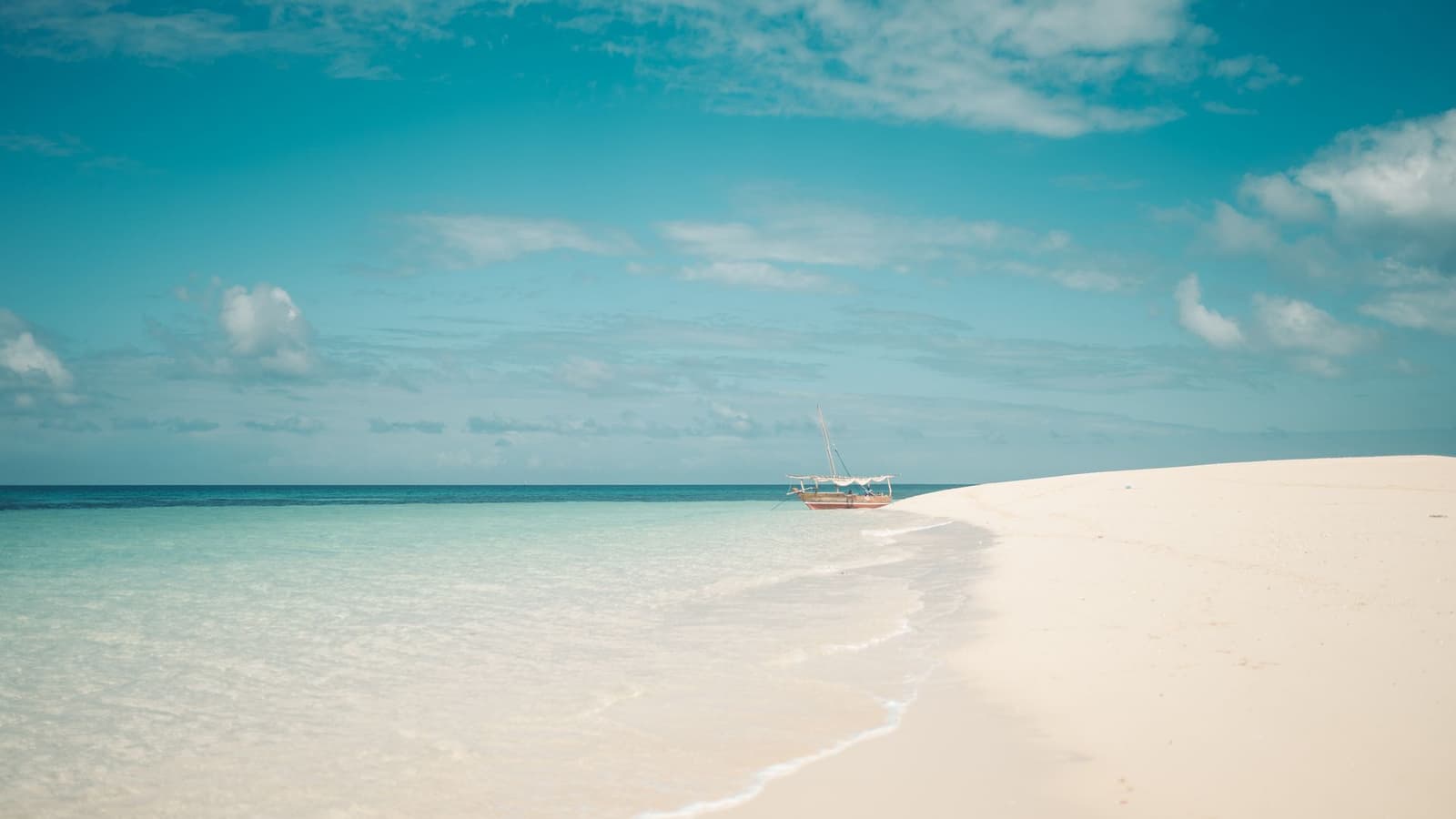 White sand beside the sea with a dhow in the distance